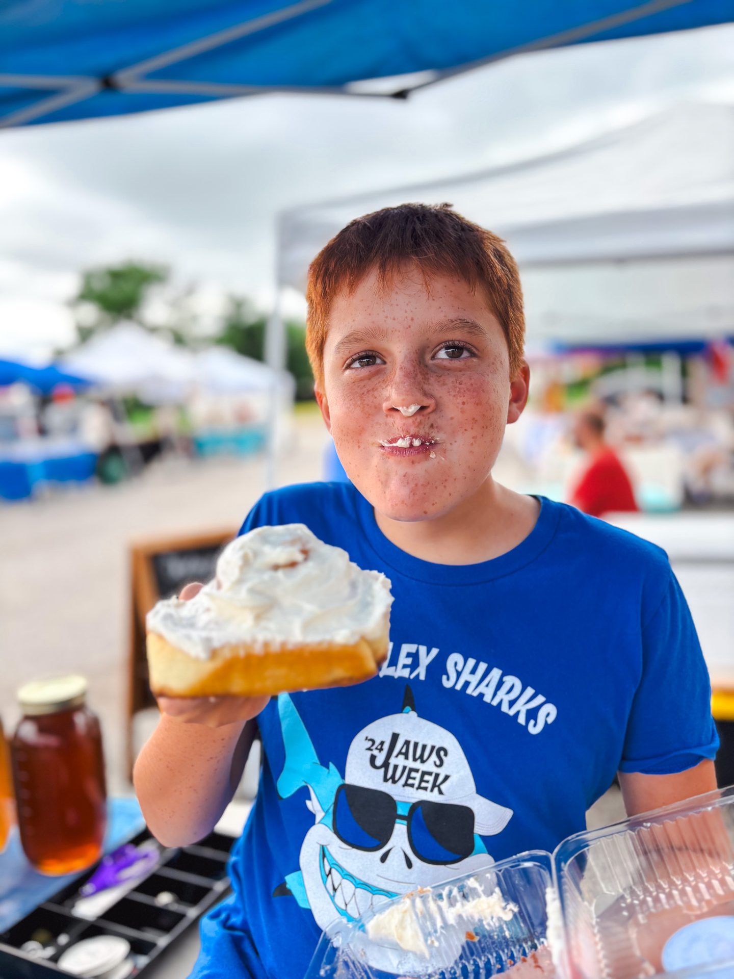 A Young red headed boy eating a cinnamon roll at the New Melle Country Market
